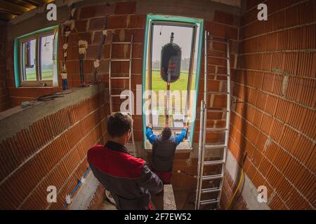 Due lavoratori maschi che installano una moderna finestra di vetro in una nuova casa che viene costruita utilizzando un sollevatore idraulico o una gru montata su un camion. Installazione moderna Foto Stock