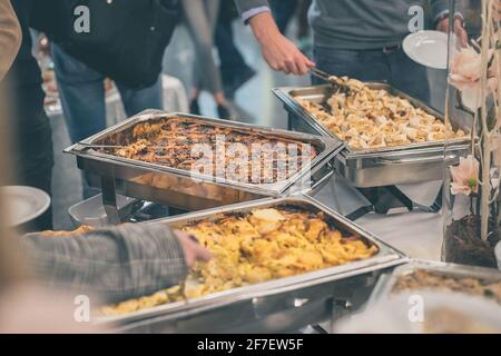 Mani di persone che hanno visto prendere il cibo da contenitori in acciaio inossidabile ad un buffet o un evento di gala di catering. Piatti gustosi serviti in occasione di un evento di catering. Foto Stock