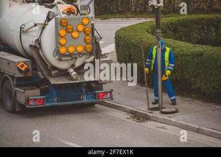 Pulizia dei tubi di scarico di foglie e detriti con un grande carrello con serbatoio del vuoto. L'acqua di pulizia del lavoratore irriconoscibile si svuota sulla strada. Foto Stock