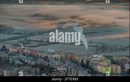 Panorama della città di Postojna in Slovenia in prima mattina d'inverno con fumo che si alza da un camino di riscaldamento su un blocco o case vicino. Hea Foto Stock