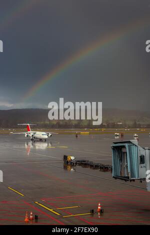 Rainbow sta sorgendo sul grembiule dell'aeroporto internazionale di Zurigo con uno dei jet planes che si avvicina alle porte. Foto Stock