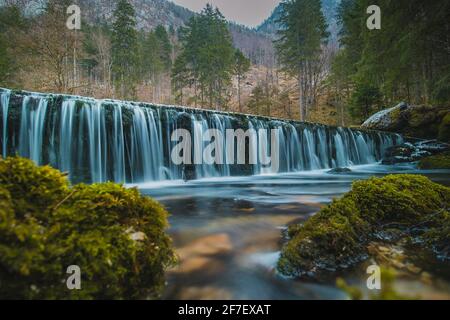 Piccola diga d'acqua presso la sorgente del fiume Kamniska Bistrica in Slovenia in inverno secco. Fredda cascata incantata con acqua corrente nel mezzo di Foto Stock