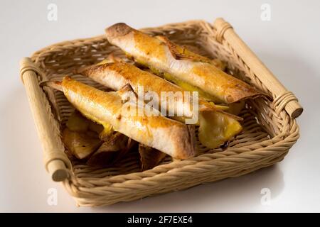 Lotto di taquitos appena sfornati in un cesto di vimini che serve, su uno sfondo bianco isolato. Gustoso spuntino messicano appena sfornato. Vista laterale Foto Stock