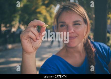 Una giovane donna caucasica che tiene una noce e la guarda mentre si gode il sole in un parco a Budapest, Ungheria mentre indossa una camicia blu. Foto Stock