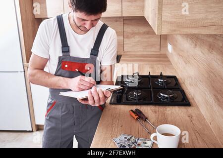 L'idraulico in uniforme firma un contratto per servizi nel cucina Foto Stock