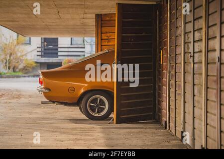 La vecchia auto d'epoca marrone è parcheggiata in un parcheggio con box auto in legno. La parte posteriore dell'auto è visibile entrando in garage in zona suburbana. Foto Stock