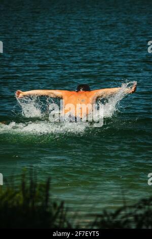 Un uomo ha visto nuotare colpo di farfalla dalla parte posteriore, sul lago vicino a Kiev, Ucraina, in una giornata di sole. Foto Stock