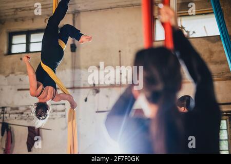 Una danzatrice da ginnastica aerea femminile su corda di seta che si esibisce in un ambiente indistrale di un laboratorio o magazzino abbandonato. Foto Stock