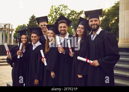 Gruppo di studenti laureati in abiti di laurea vicino al campus universitario. Foto Stock