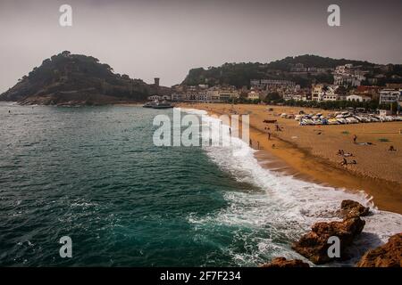 Panorama della spiaggia di Tossa de Mar, vicino a Lloret de mar in Catalunya, le onde e la spiaggia sabbiosa con la città sullo sfondo sono visibili. Foto Stock