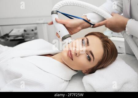 Cosmetologa che fa una terapia acustica dell'onda per il viso della donna. Ringiovanimento della pelle con onde acustiche, primo piano Foto Stock