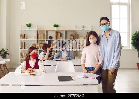 Insegnante che abbraccia studente in classe con altri ragazzi e. ragazze che si siedono alle scrivanie Foto Stock