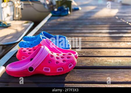 Infradito rosa e blu sul molo in legno mattina presto coperta da rugiada con luce solare offuscata il lago sullo sfondo Foto Stock