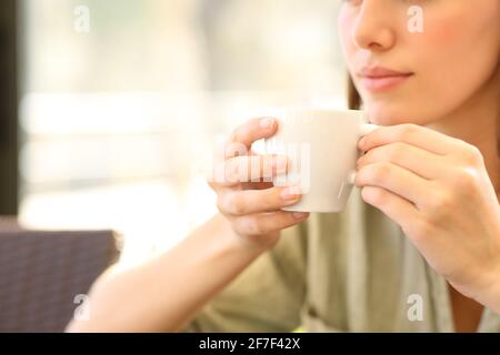 Primo piano di una donna che tiene la tazza di caffè seduto in un bar una giornata di sole Foto Stock