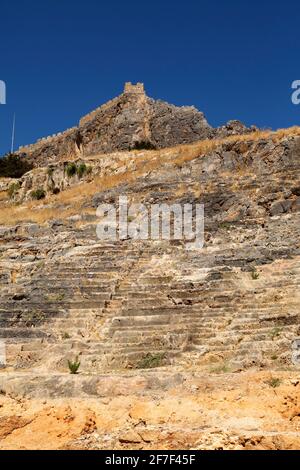 Posti a sedere nell'antico teatro ai piedi dell'Acropoli lidiana di Lindos, a Rodi, Grecia. Il locale è stato utilizzato come luogo di intrattenimento. Foto Stock