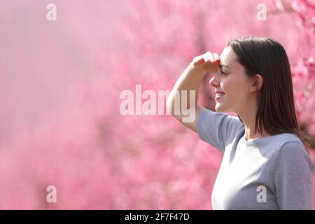 Vista laterale ritratto di una donna felice in cerca di guardare via proteggere dal sole con la mano in una fiorita rosa campo Foto Stock