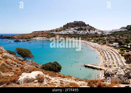 Ombrelloni sulla spiaggia di Lindos a Rodi, Grecia. L'Acropoli di Lindian sorge su case bianche nel villaggio di pescatori. Foto Stock