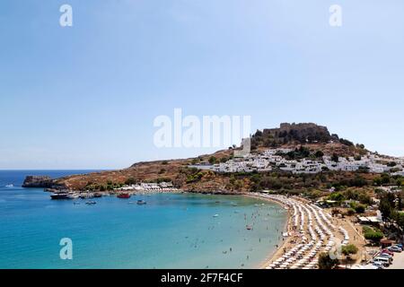 Ombrelloni sulla spiaggia di Pallas a Lindos a Rodi, Grecia. L'Acropoli di Lindian sorge su case bianche nel villaggio di pescatori. Foto Stock