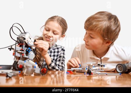 Vista frontale dei bambini che si divertono, creando giocattoli. Ingegneria scientifica. Bella amici interessati sorridendo, chattando, ragazza mostrando robot ragazzo fatto con interessante kit di costruzione per bambini sul tavolo. Foto Stock