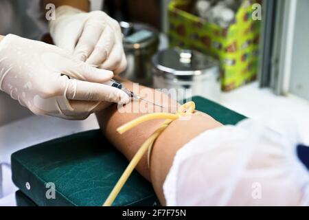 Il medico o l'infermiere indossano guanti bianchi medici utilizzando una siringa per ago per prelevare un campione di sangue dal braccio del paziente in ospedale. Foto Stock