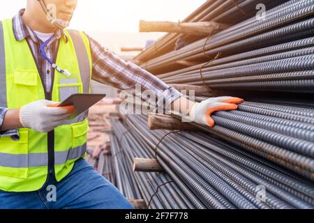 Primo piano di un ingegnere della costruzione o di un lavoratore che utilizza un tablet controllare l'acciaio di qualità per fondazioni in calcestruzzo e verificarne la qualità di barra rotonda a strutt Foto Stock