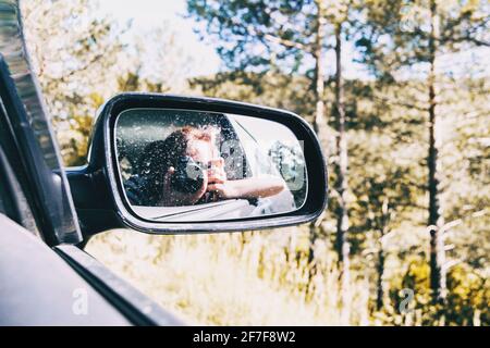 Selfie di una ragazza nella vista posteriore della macchina mentre la macchina è in funzione. La ragazza indossa i capelli legati e la soffia via con il vento. Foto Stock