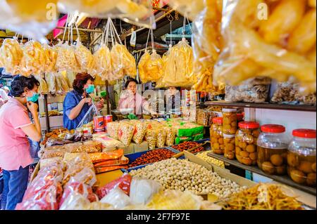 Chinatown, Bangkok – 14 novembre 2020: Due clienti che indossano maschere facciali si trovano di fronte a un negozio di alimentari, che vende varietà di prelibatezze disidratate. Foto Stock