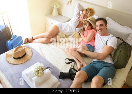Genitori e figlia in vacanza con la famiglia che si trovano in un hotel letto guardando dritto davanti sorridendo con valigie e oggetti da viaggio Foto Stock