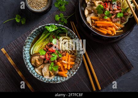 Zuppa di ramen in stile asiatico con noodle udon, manzo, shiitake, cavolo pak choi e carote su sfondo nero Foto Stock