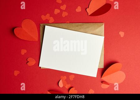 Biglietto d'auguri o invito vuoto. San Valentino carta mockup con cuori di carta su sfondo rosso Foto Stock