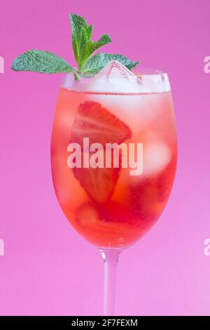 Primo piano su una bevanda con fragole e ghiaccio in un vino vetro su sfondo rosa Foto Stock