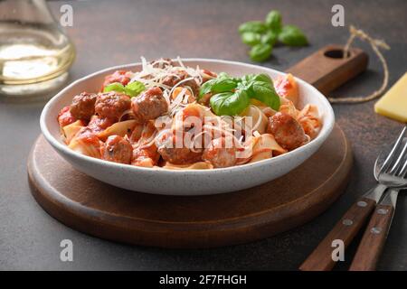 Fettuccine di pasta con polpette, parmigiano, pomodori, basilico su fondo marrone. Primo piano. Foto Stock