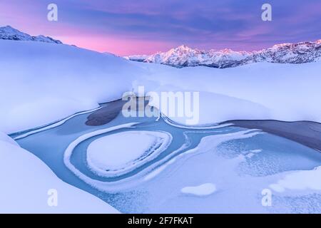 Forma pazzesca in un lago alpino ghiacciato all'alba con vista sul Monte Disgrazia, Valmalenco, Valtellina, Lombardia, Italia, Europa Foto Stock