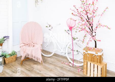 Retro bicicletta e poltrona in vimini sotto coperta con fiori sullo sfondo di casa bianca girato dal fronte al cortile posteriore. Decorazioni nel giardino in stile provenzale Foto Stock