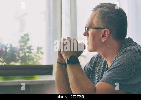L'uomo singolo soffre di solitudine o depressione. L'uomo è seduto nel soggiorno al tavolo Foto Stock