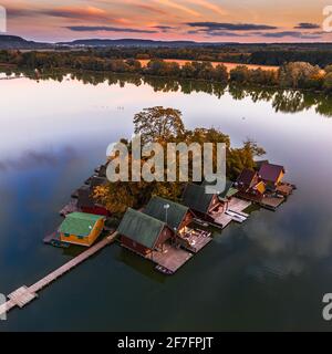 Tata, Ungheria - bellissimo tramonto autunnale su case di pesca in legno su una piccola isola al Lago Derito (Derito-to) nel mese di ottobre con cielo dorato e autum Foto Stock