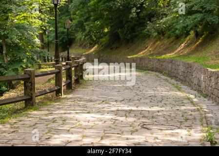 Un sentiero lastricato in pietra che scende dalla montagna. Percorso in pietra e muro. Recinzione di legno fatta di travi spesse. Foto Stock