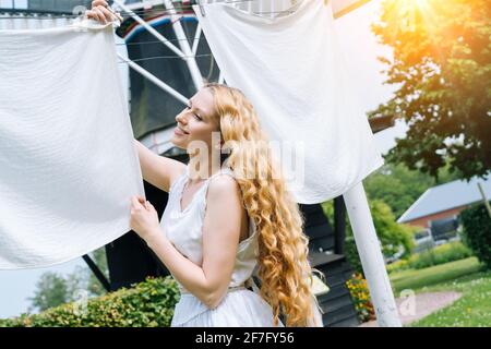 Donna vestita con abiti tradizionali olandesi scarpe in legno zoccoli gialli appesi vestiti sulla stendibiancheria all'esterno. Lavanderia che asciuga all'aperto Olanda Windmill sfondo al sole ventoso giorno. Stile retrò vintage Foto Stock