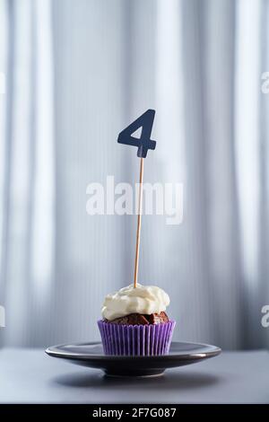 Concetto di biglietto d'auguri minimalistico per anniversario o compleanno. Gustoso cupcake al cioccolato o muffin fatti in casa con crema di condimento e numero 4 quattro su piatto nero e sfondo luminoso. Immagine di alta qualità Foto Stock