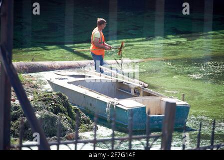 Un uomo in un giubbotto arancione di segnalazione libera il fango dal fiume. Nelle vicinanze è presente una barca. Foto Stock