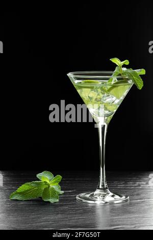 Delizioso cocktail verde rinfrescante con ghiaccio, foglie di menta piperita e fette di lime su una superficie di pietra nera Foto Stock