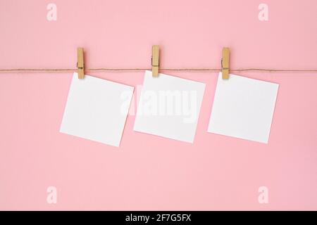 Foglio di carta vuoto per note, cornici appesi su corda con stendibiancheria e isolate su sfondo rosa. Bianco vuoto con spazio vuoto per il testo. Foto Stock