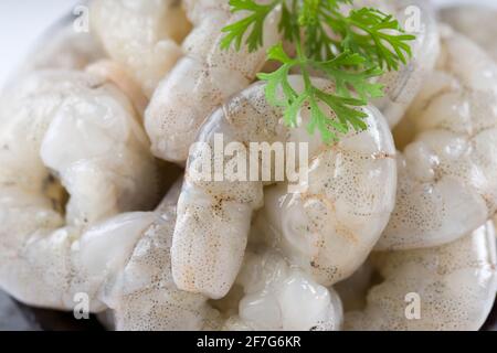 Gamberi o gamberetti pelati grezzi disposti in ceramica nera pentola piccola e guarnita con foglia di coriandolo che è pronta per cucinare, messo su un bianco testurizzato Foto Stock