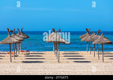 Ombrelli di paglia sulla spiaggia nella giornata di sole sotto il cielo di lue come mare Mediterraneo sullo sfondo a Palma, Spagna. Foto Stock