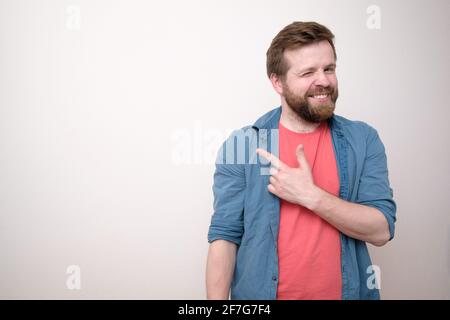 L'uomo sorridente, positivo, punta il dito indice di lato e sembra favorevole. Spazio di copia. Sfondo bianco. Foto Stock