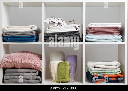 Pile di asciugamani, lenzuola, lenzuola, coperte e cuscini su un ripiano bianco. Foto Stock
