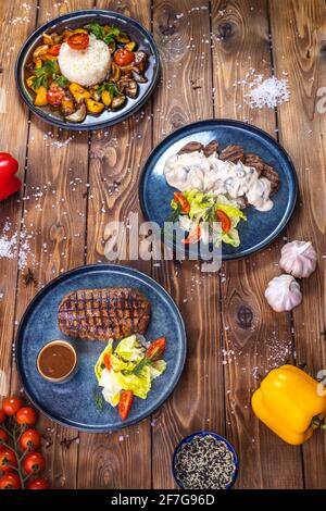 Bistecca con salsa, lattuga, rosmarino, pomodori ciliegini su tavola di legno. Layout piatto. Foto Stock