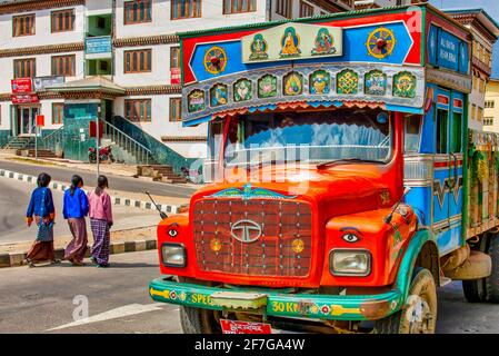 Le donne nella tradizionale Kira camminano vicino ad un camion dipinto di Tata a Thimphu, Bhutan Foto Stock