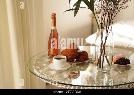 Tavolo in vetro con una tazza di caffè, croissant dolci. Bottiglia di vino e bicchieri Foto Stock