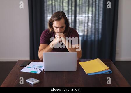 Preoccupato uomo caucasico seduto al tavolo che lavora da casa e. guardando lo schermo del notebook Foto Stock